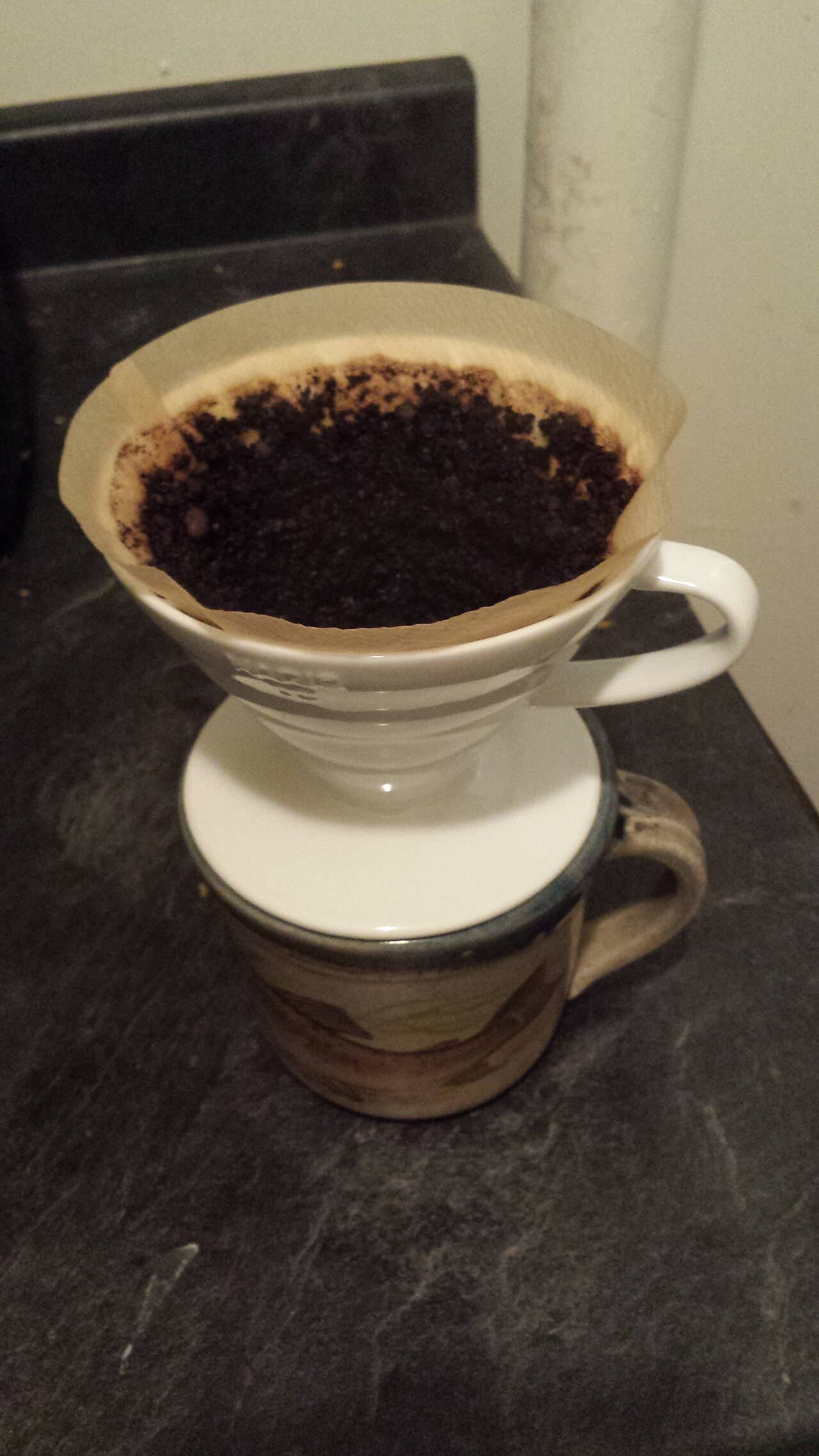 Ampas kopi di dalam filter kertas pada corong V60 di atas cangkir.