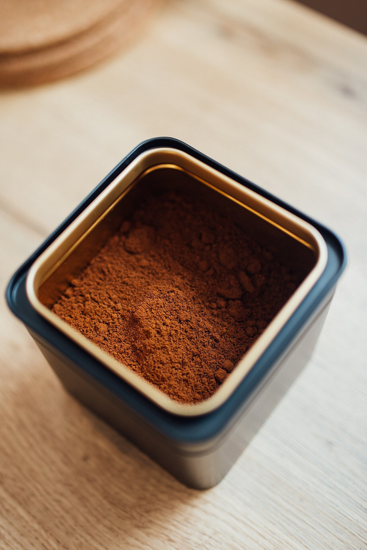 Kopi bubuk halus dalam wadah hitam terbuka di atas meja kayu.