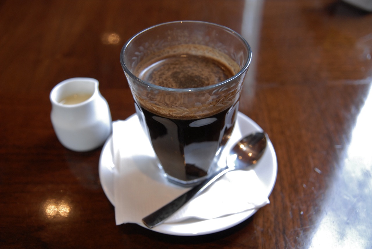 Kopi tubruk dalam gelas dengan butiran ampas di permukaan.